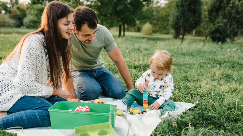 Les parents regardent leur petit enfant jouer avec des jouets de voiture à l'extérieur