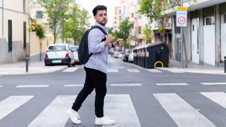 Un jeune homme traversant un passage pour piétons tenant une tasse de café