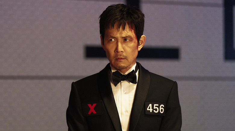 Gi-Hun porte un smoking et est assis à une table de dîner dans Squid Game Saison 3