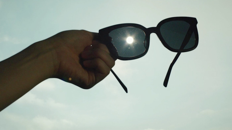 Une main tenant une paire de lunettes de soleil (avec le soleil au milieu) en parasite