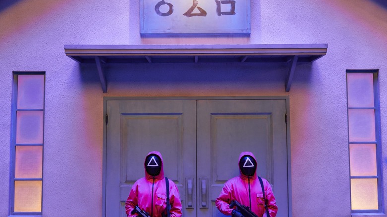 Gardes masqués debout sur un sol de jeu dans le jeu de calmar