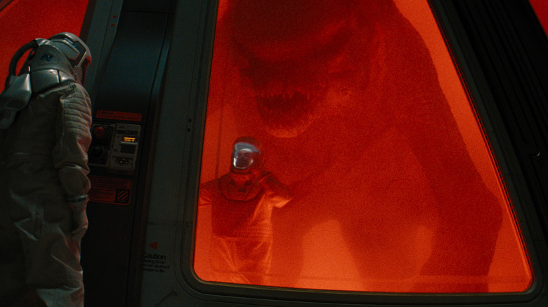 Le D-Rex se silhouette par des feux rouges se faufilant derrière un scientifique à une porte explosive dans Jurassic World Rebirth