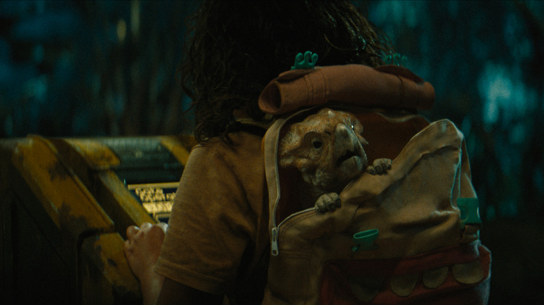 Audrina Miranda en tant qu'Isabella Delgado transportant un bébé dinosaure nommé Dolores dans son sac à dos dans Jurassic World Rebirth