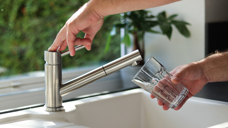 Gros plan des mains mâles versant de l'eau du robinet dans un verre dans la cuisine