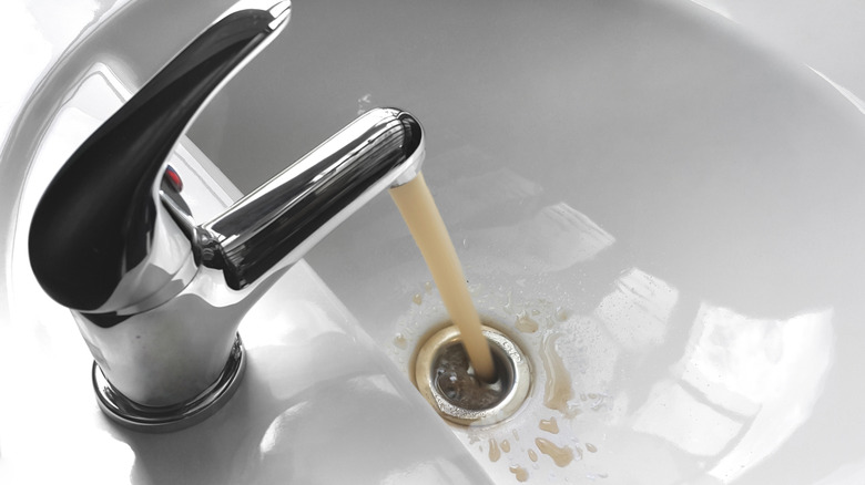 L'eau sale coule d'un robinet dans un évier de salle de bain blanc