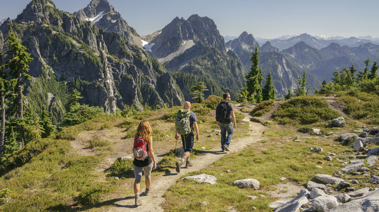 Trois randonneurs marchent le long d'un chemin avec des montagnes en arrière-plan.