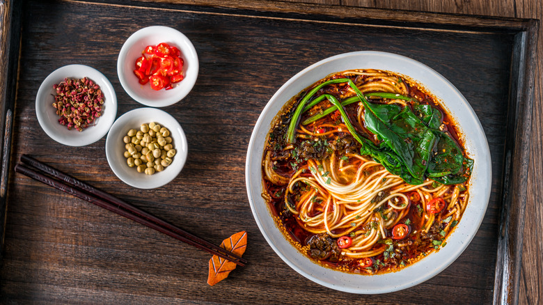 Des bols de nouilles et d'autres ingrédients se tiennent sur une table avec des baguettes
