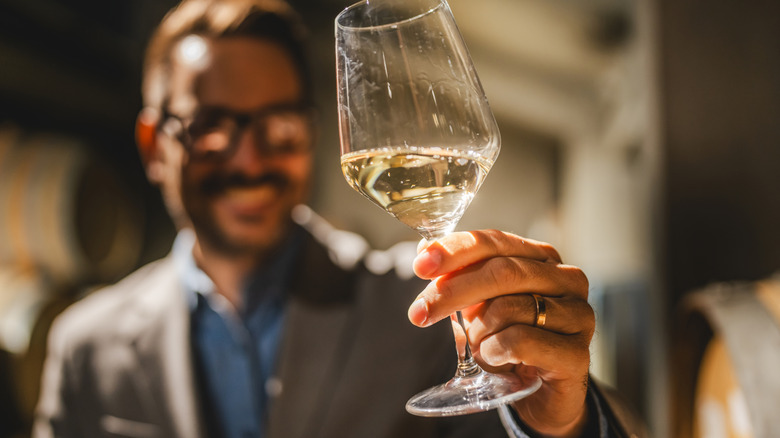 Un verre à vin au centre du premier plan tandis qu'un homme en arrière-plan l'examine.