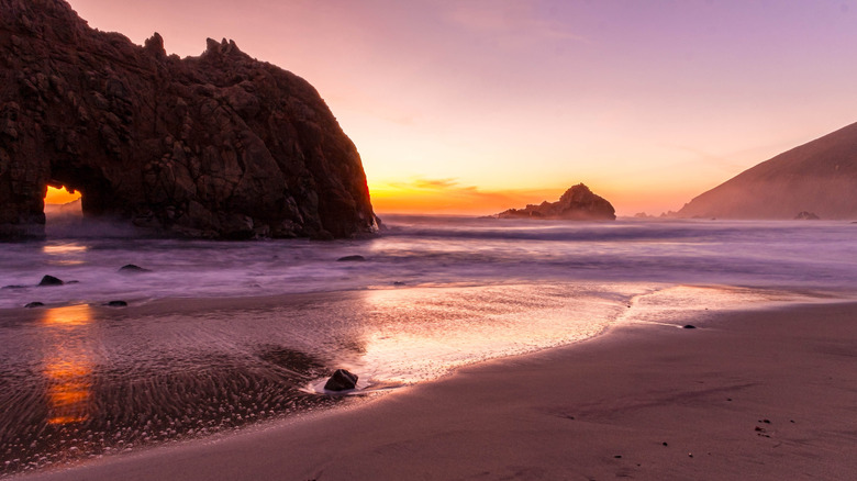 Un soleil dramatique baigne le sable dans les tons de violet à Pfeiffer Beach, Big Sur, Californie