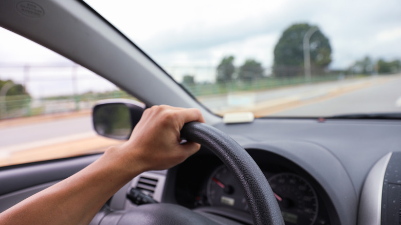 Une main saisit un volant dans une voiture qui roule sur la route