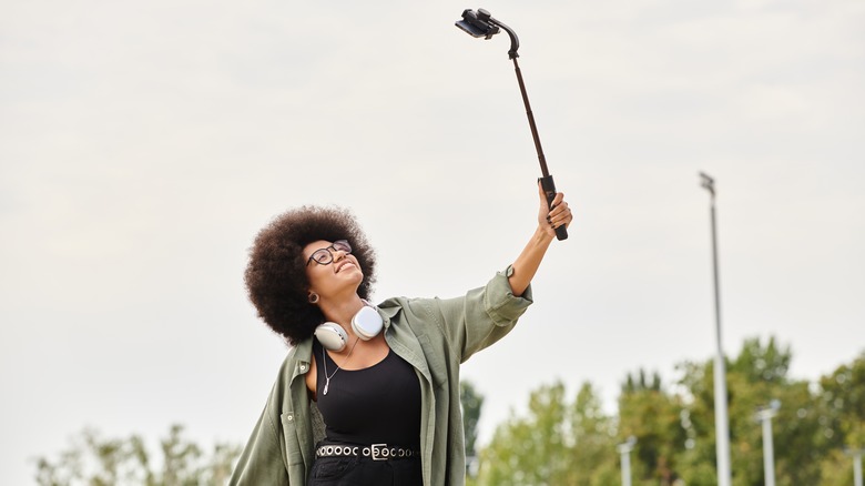 Une femme utilise un bâton de selfie pour prendre un autoportrait à l'extérieur