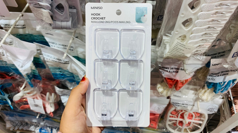 Une main tenant un paquet de crochets adhésifs dans un magasin.