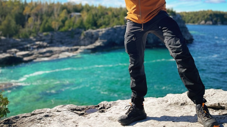 Personne en pantalon de randonnée sur roche surplombant l'eau