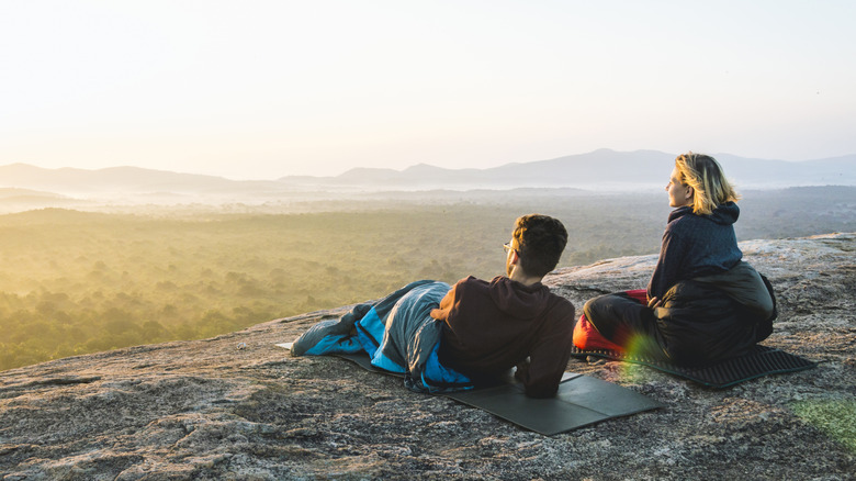 Des gens dans des sacs de couchage sur un rocher au lever du soleil.