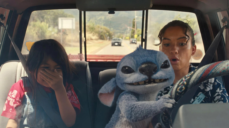 Stitch prend le volant de la voiture tandis que Nani halète sous un choc et Lilo couvre son visage en riant 