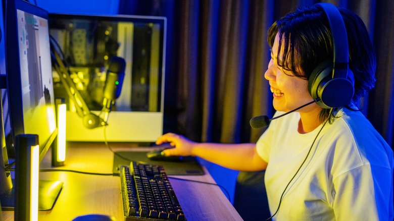 Une personne riant tout en portant des écouteurs à un bureau avec un PC et un moniteur