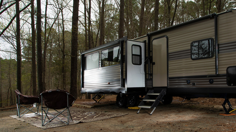 Le camping avec VR et chaises en forêt avec le côté de la RV a glissé