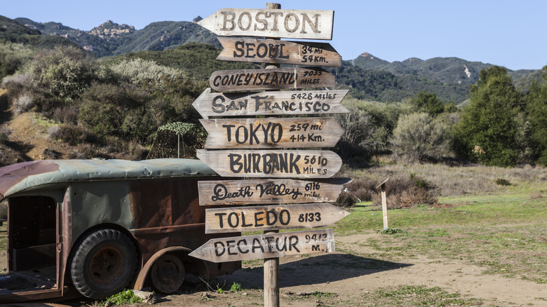 Place en bois signe ensemble sur un poteau avec un véhicule rouillé à côté
