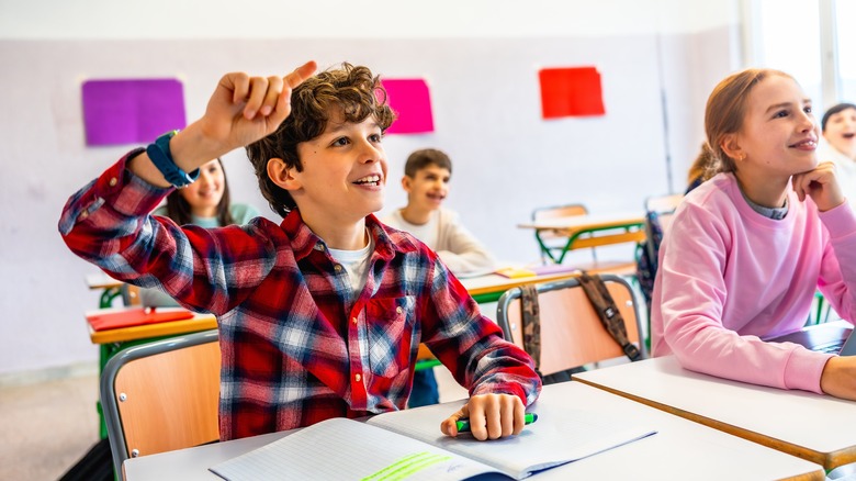 Enfant levant la main en classe pour répondre à une question