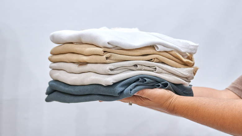 Un ensemble de mains tenant un tas de chemises de couleur claire repliées