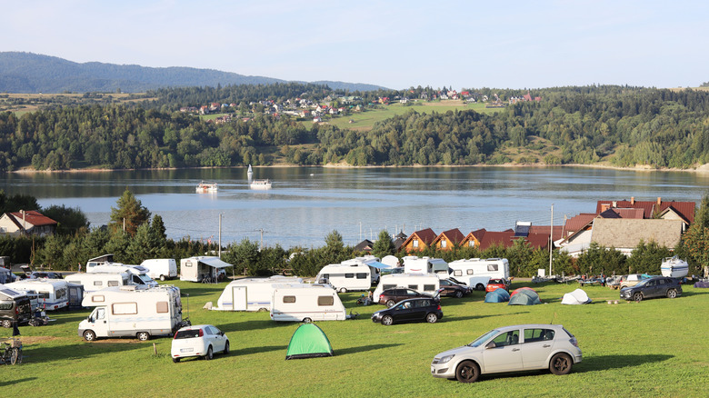Un camping avec un lac et des collines en arrière-plan avec des voitures et des remorques garées