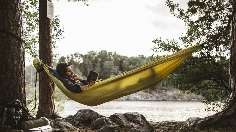 La personne est assise dans son hamac dans les bois en lisant