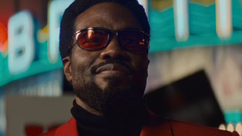 Wonder Man portant des lunettes de soleil rouges, un costume rouge et un col roulé noir tout en regardant quelqu'un hors écran