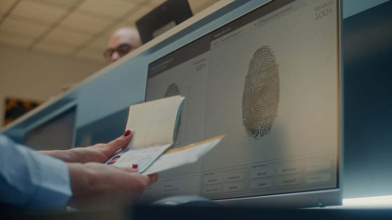 Mains comparant un passeport à un écran d'ordinateur avec une empreinte digitale dessus.