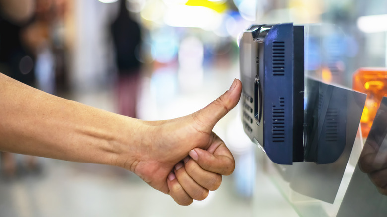 Une main tenant le pouce jusqu'à un scanner de sécurité.