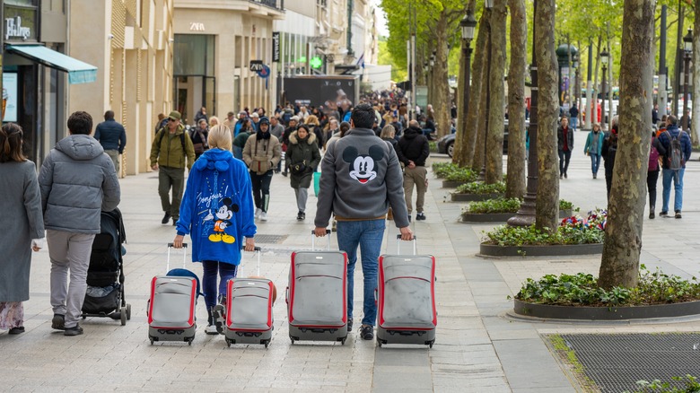 Deux personnes dans les sweat-shirts Disney marchant avec des valises