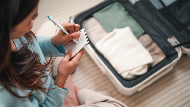 Femme qui fait une liste d'emballage sur sa valise