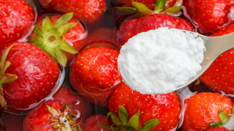 Cuillerée de bicarbonate de soude maintenue sur un bol de fraises et d'eau