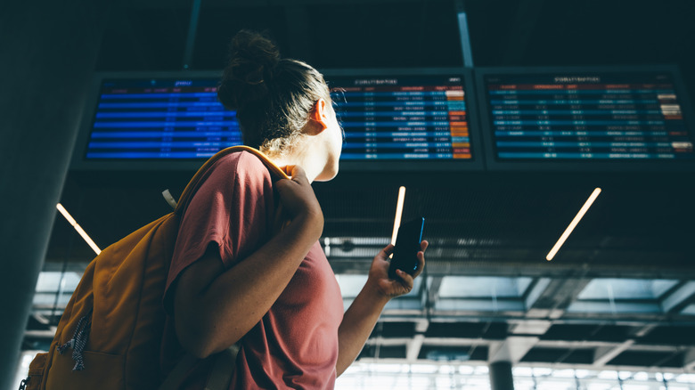 Une femme vérifiant le conseil d'administration des compagnies aériennes dans un aéroport.