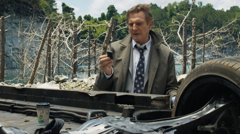 Frank Drebin à côté d'une voiture renversée dans le pistolet nu (2025)