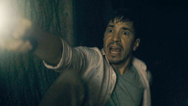 AJ, l'air effrayé, maintient une lampe de poche dans un sous-sol sombre en barbare