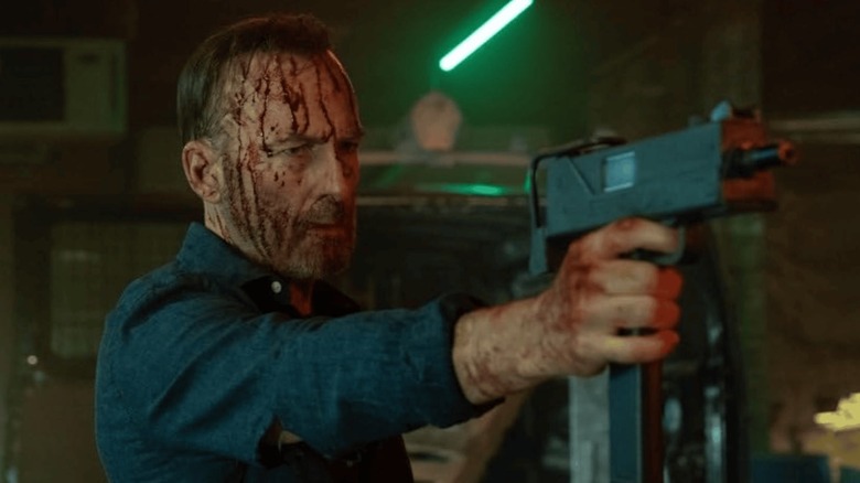 Bod Odenkirk comme Hutch tenant une mitrailleuse ensanglantée dans Nobody 2