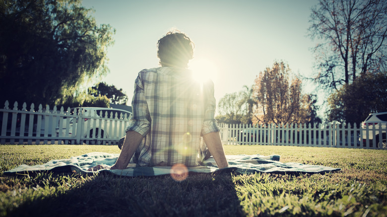 L'arrière d'une personne assise sur une couverture sur sa pelouse.