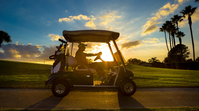 Un homme conduisant une voiturette de golf contre le soleil couchant