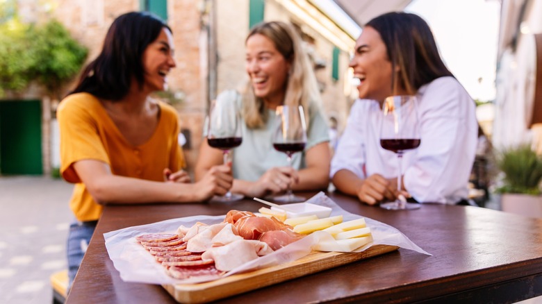 Trois femmes assises à une table en profitant d'un verre de vin rouge avec une planche de fromage