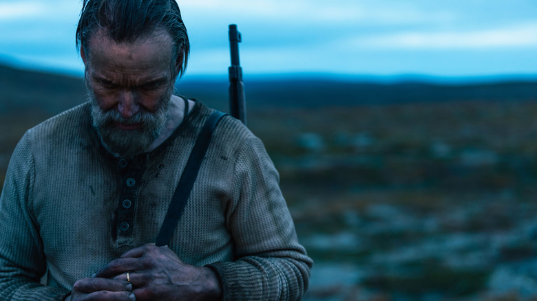 Aatami debout dans un champ au crépuscule avec un fusil sur le dos à Sisu