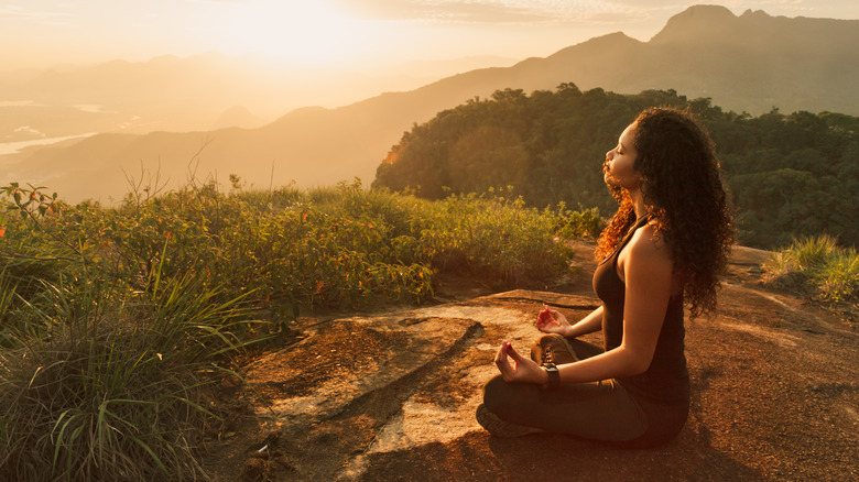 Une femme est assise en position de lotus au bord d'une montagne boisée