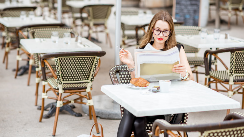 Une femme lisant un journal en fumant dans un café