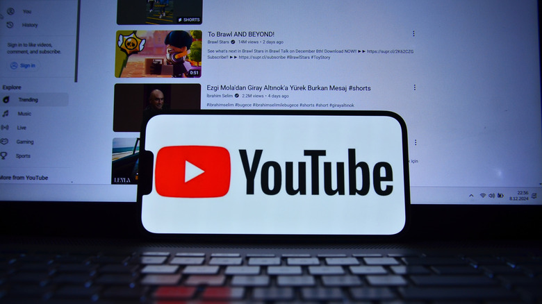 Un smartphone montrant le logo YouTube à l'écran, la page d'accueil de YouTube en arrière-plan.