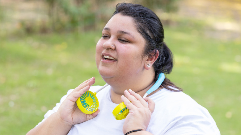 Femme utilisant un ventilateur de cou pour se rafraîchir