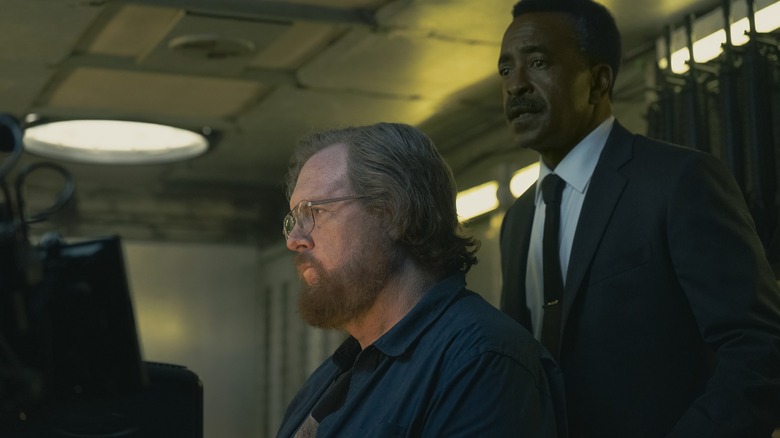 Steve Agee en tant que John Economos qui regardait un aperçu de Tim Meadows que Langston Fleury regarde dans la saison 2 Peacemaker