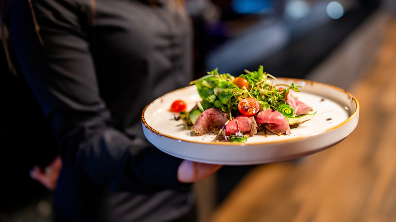 Personne tenant une assiette de salade gastronomique avec du thon poêlé