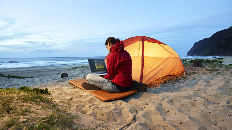 Une dame assise près d'une tente avec un ordinateur portable