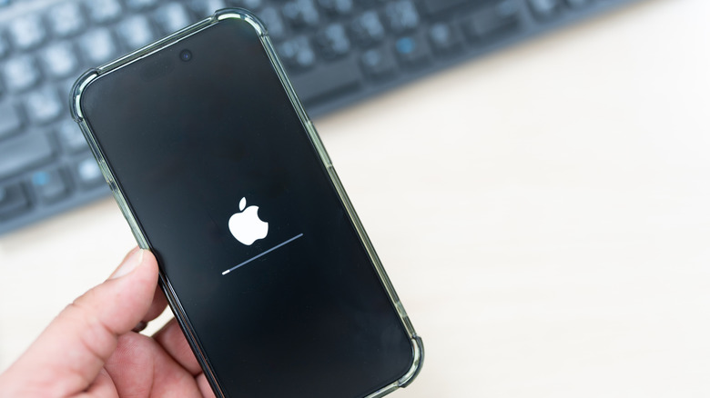 Main gauche redémarrant iPhone avec clavier noir en arrière-plan flou