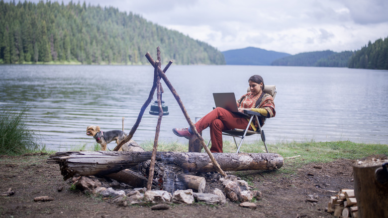 Jeune femme prenant son café du matin et utilisez un ordinateur portable pour travailler à distance alors qu'il était sur une femme Cayoung en train de prendre son café du matin et d'utiliser un ordinateur portable pour travailler à distance alors que des vacances en camping