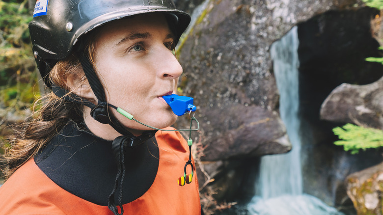Une femme casquée près d'une cascade craquette un coup de sifflet dans ses dents
